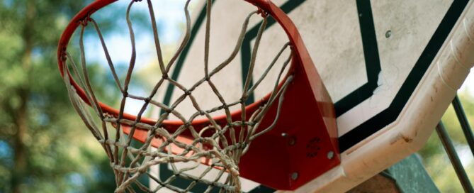 A detailed view of a basketball hoop and net against a blurred outdoor background, emphasizing a sporty feel.